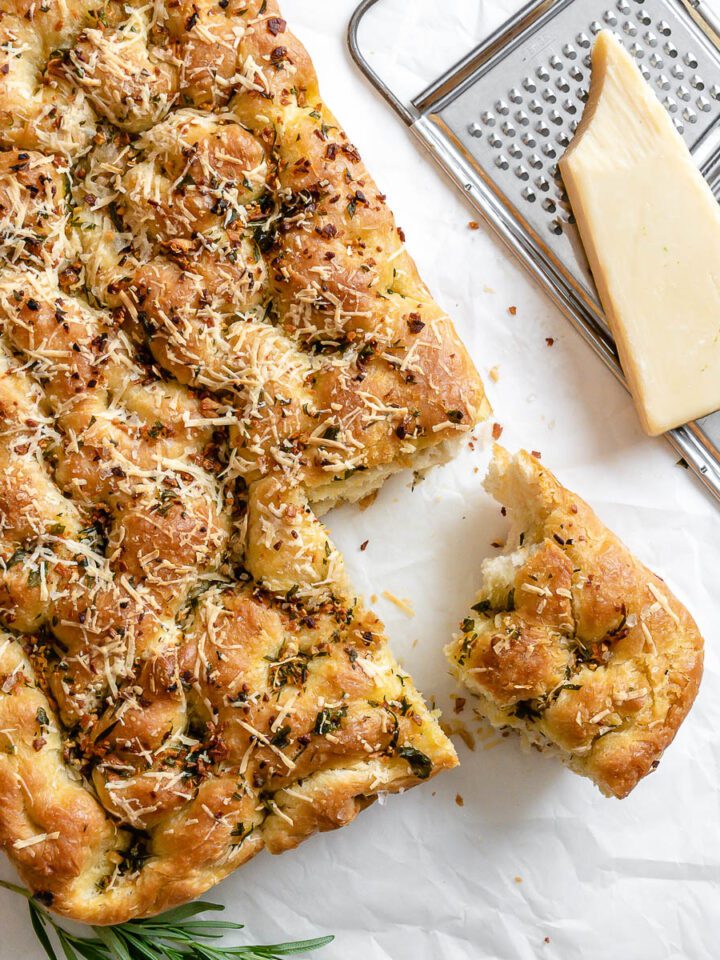 completed Vegan Cheesy Garlic Focaccia with a piece cut out against a white surface