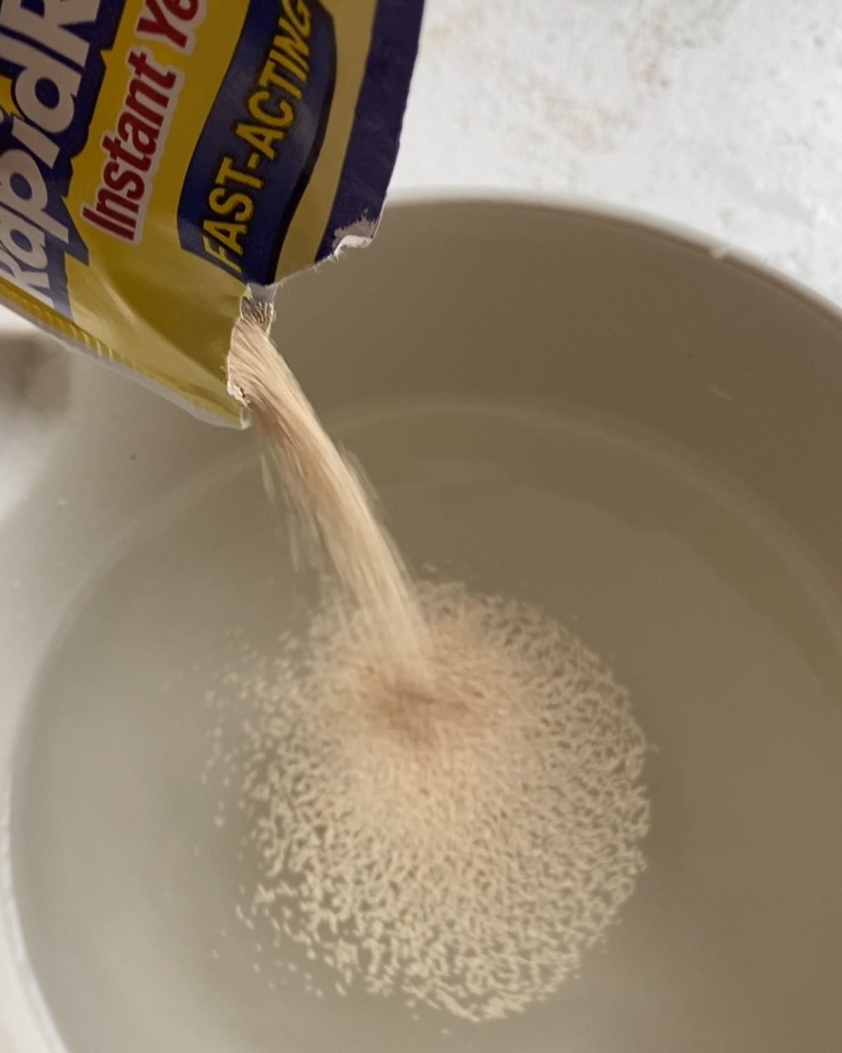 process of pouring yeast into a bowl of water