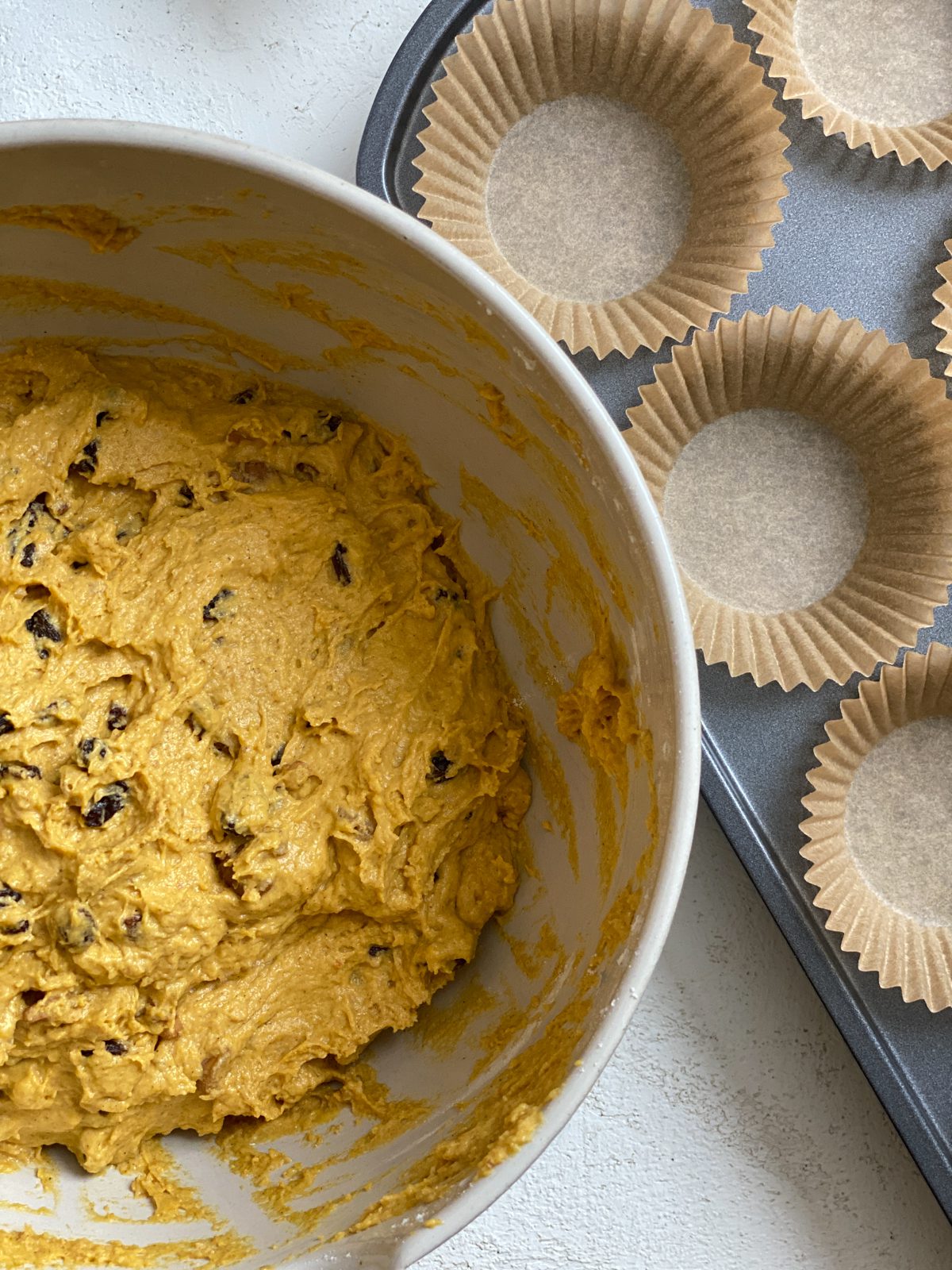 pumpkin muffins mixture alongside muffin tin with liners