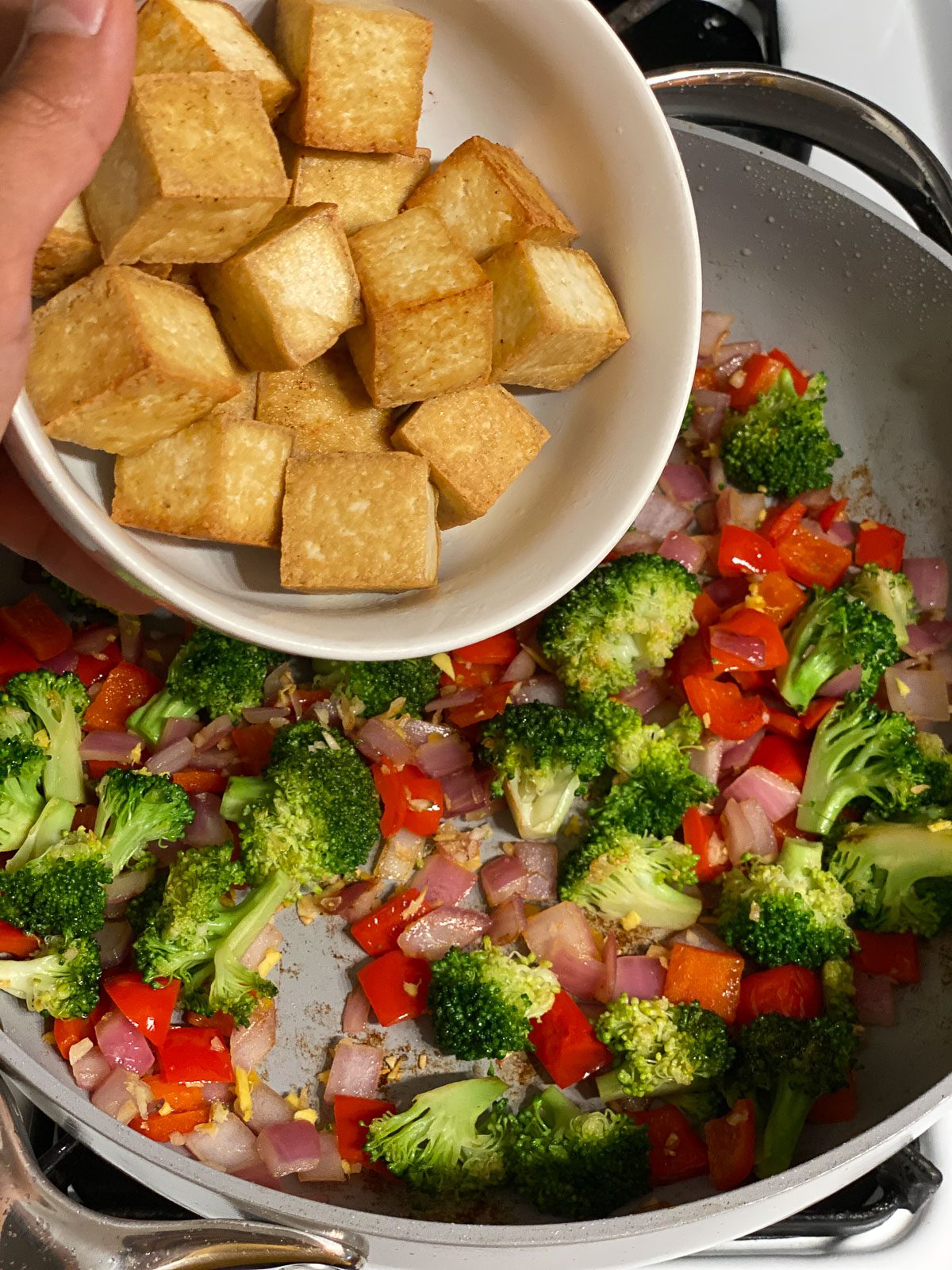 process shot of adding cooked tofu to pan of veggies