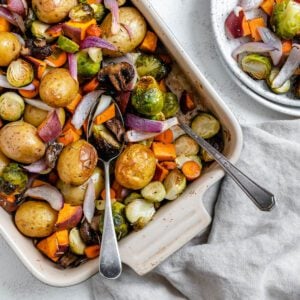 completed Roasted Vegetables in a baking dish alongside a bowl of veggies against a light surface