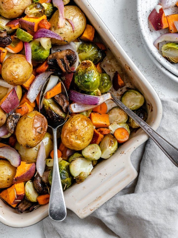completed Roasted Vegetables in a baking dish alongside a bowl of veggies against a light surface