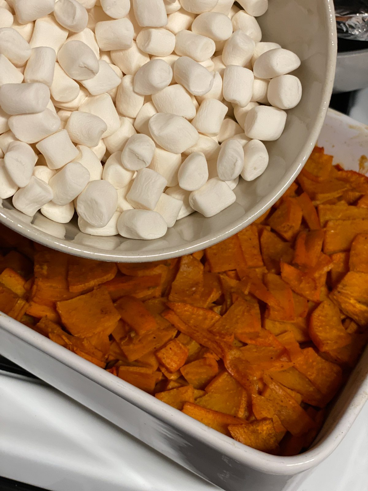 process shot of adding marshmallows to yam mixture in baking dish