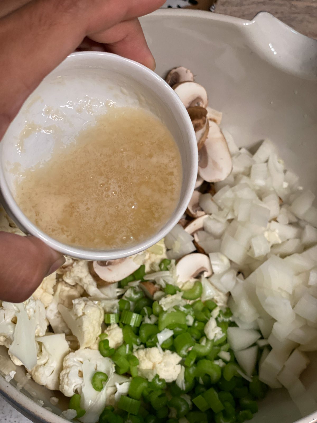 process shot of vegan butter being added to bowl of Vegan Cauliflower Stuffing ingredients