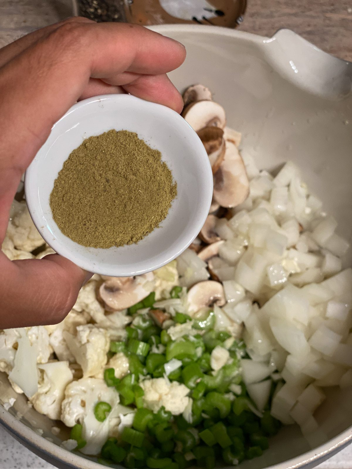 process shot of seasoning being added to bowl of Vegan Cauliflower Stuffing ingredients