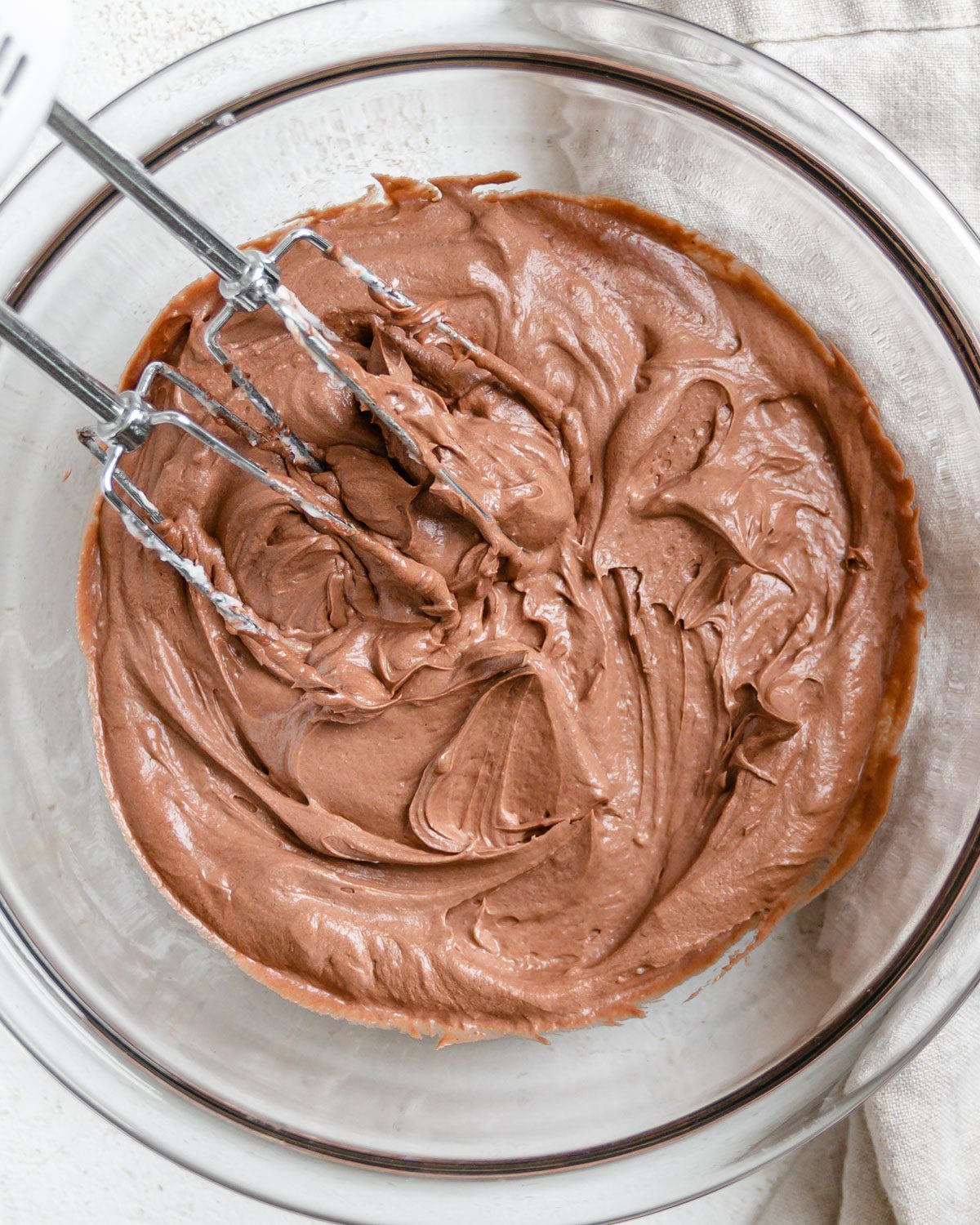 completed Vegan Chocolate Frosting in a bowl against a white background with a mixer on top