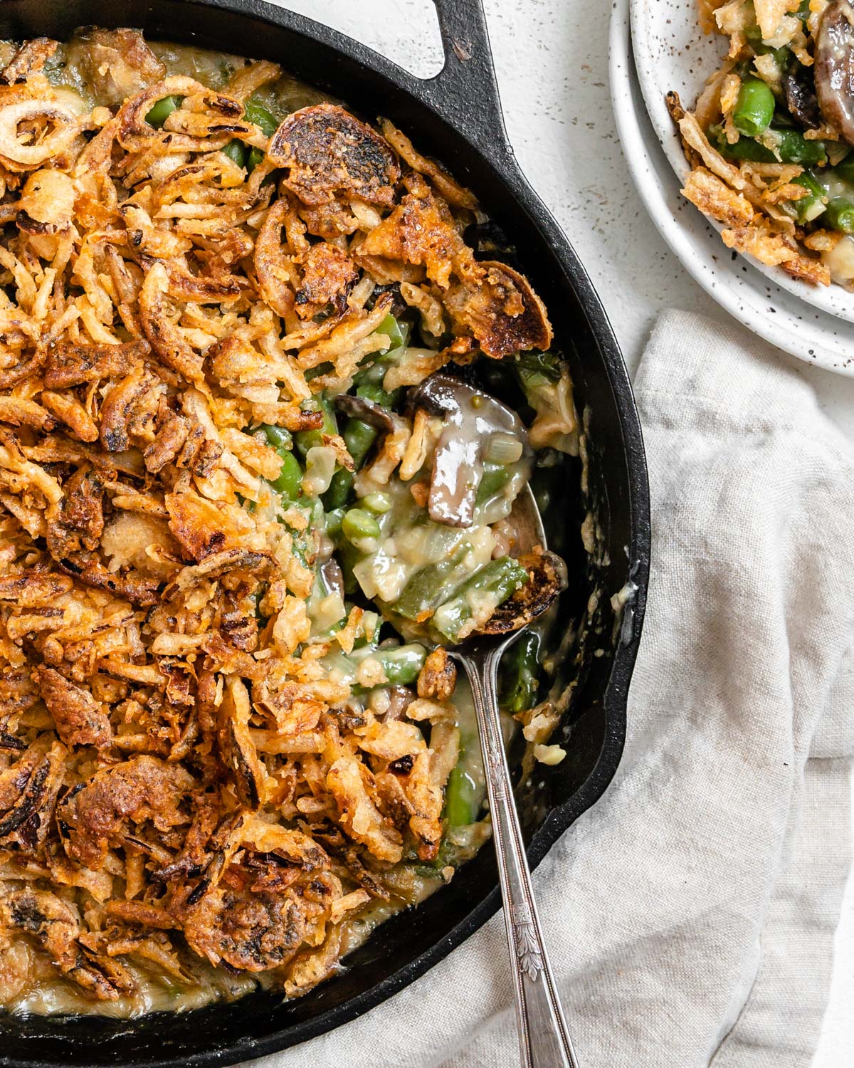 completed Dairy-Free Green Bean Casserole in a skillet with a portion plated on a white plate