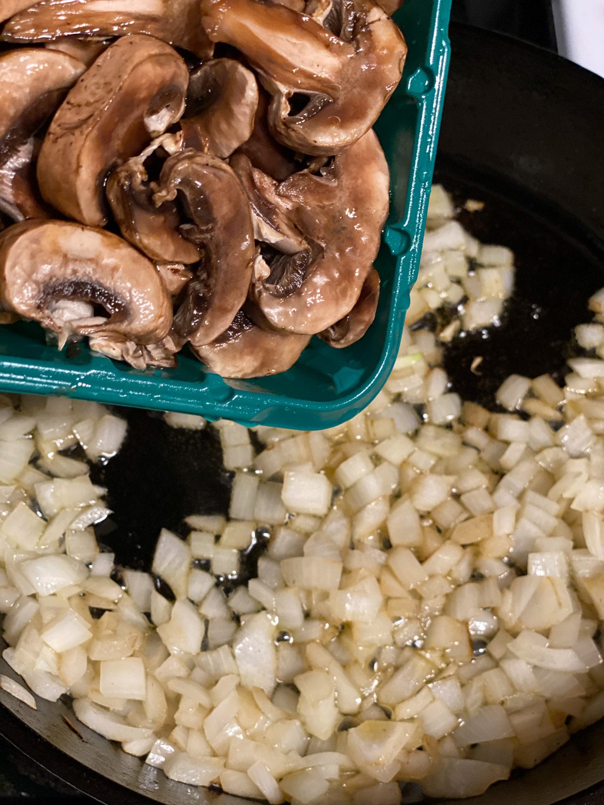 process of adding mushrooms to onion in pan