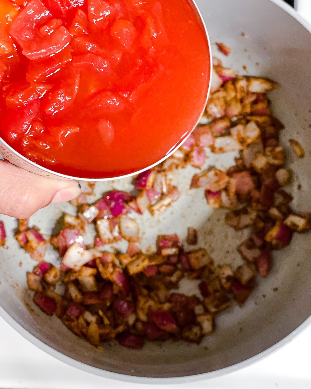 process shot of adding diced tomatoes to a pan