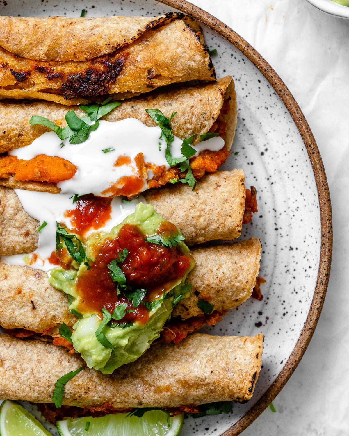 completed Vegan Taquitos against a white surface and topped with garnishes