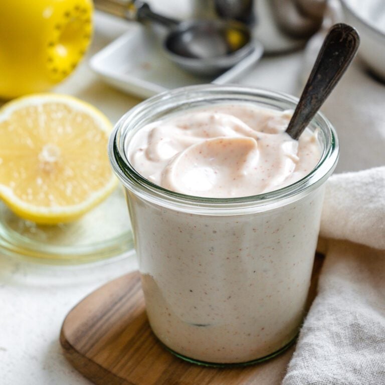 completed 5-Minute Vegan Garlic Aioli in a glass container with ingredients in the background