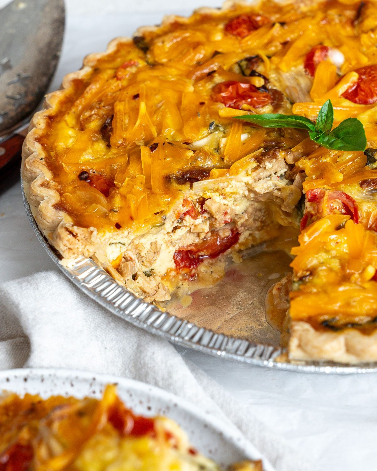 Close-up of a cut vegan Just Egg quiche showing the fluffy filling, tomatoes, and melted cheddar inside.