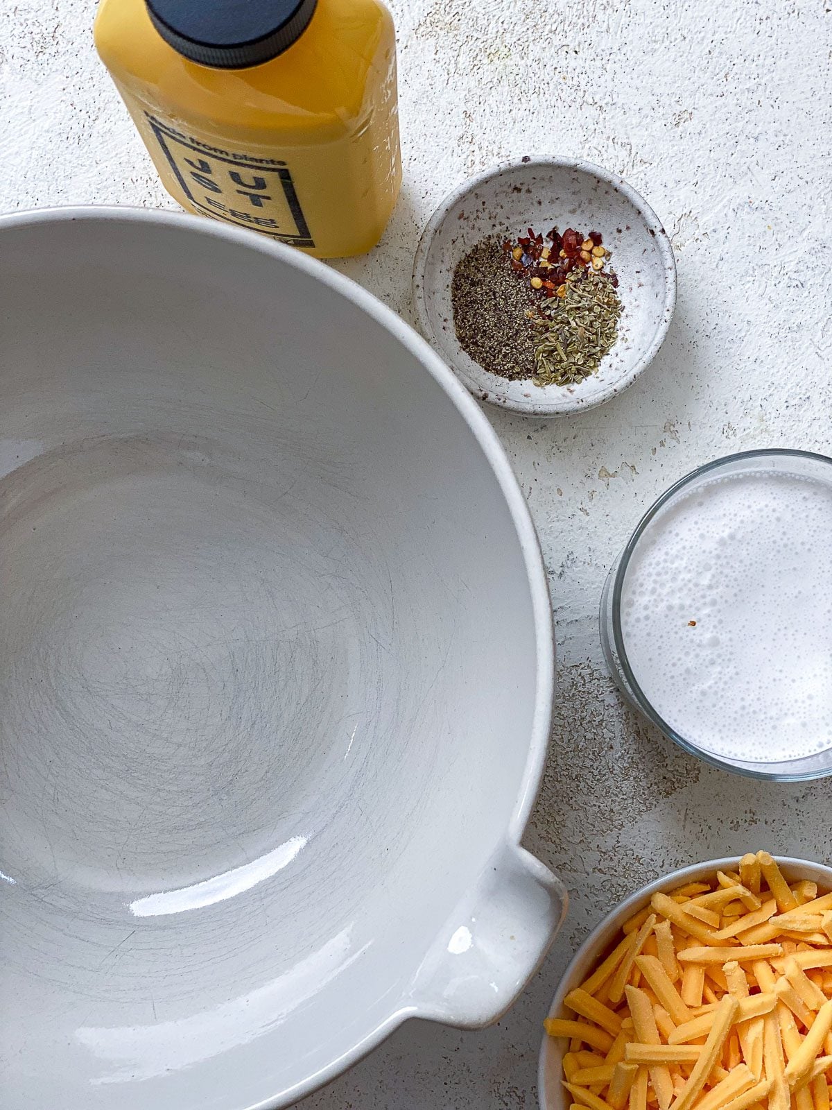A large white mixing bowl with Just Egg, vegan cream, seasonings, and shredded vegan cheddar set out around it.