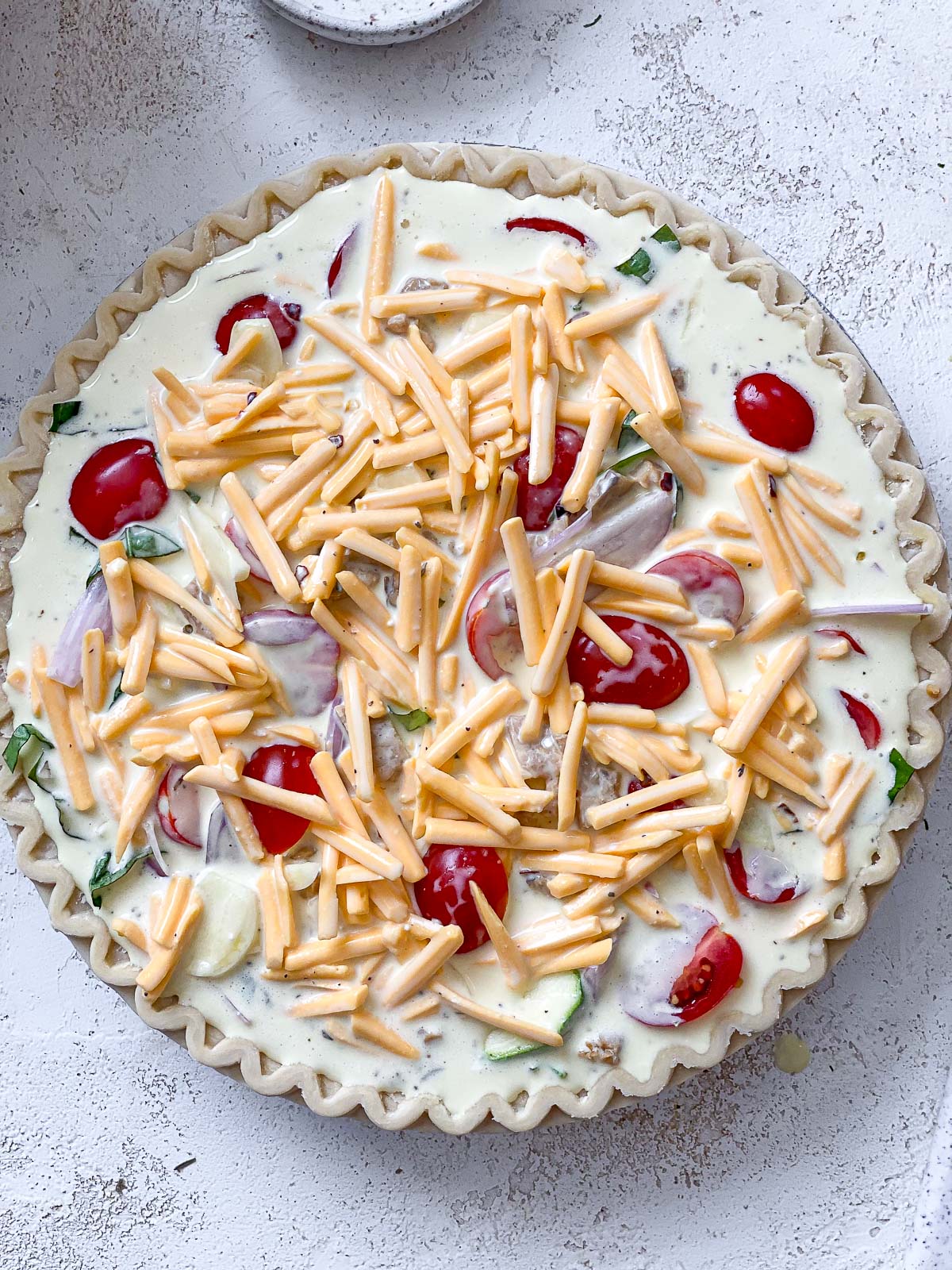 An unbaked vegan quiche filled with the Just Egg mixture and topped with shredded vegan cheddar.