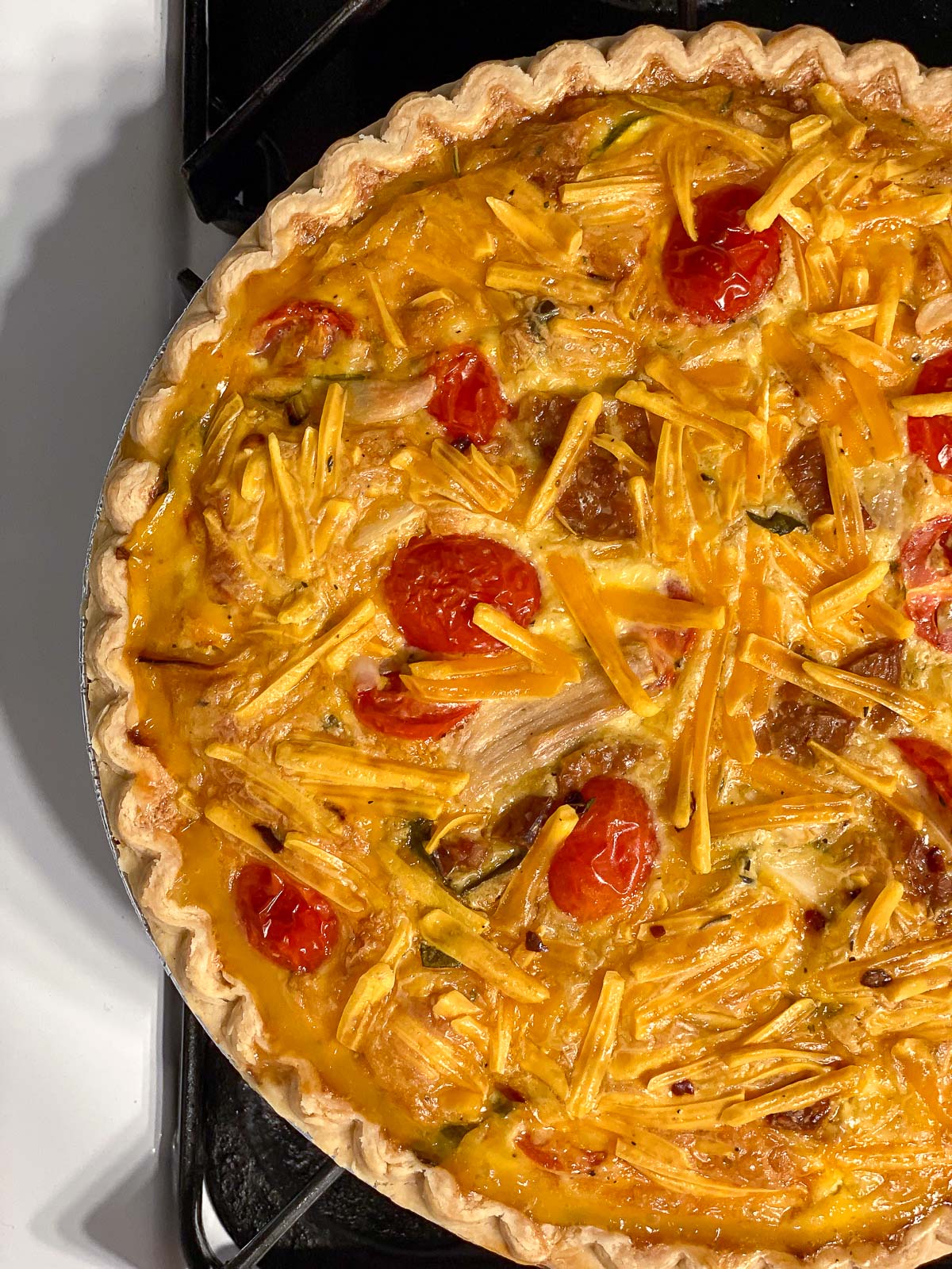A baked vegan Just Egg quiche with golden melted cheddar, cherry tomatoes, and tempeh bacon.