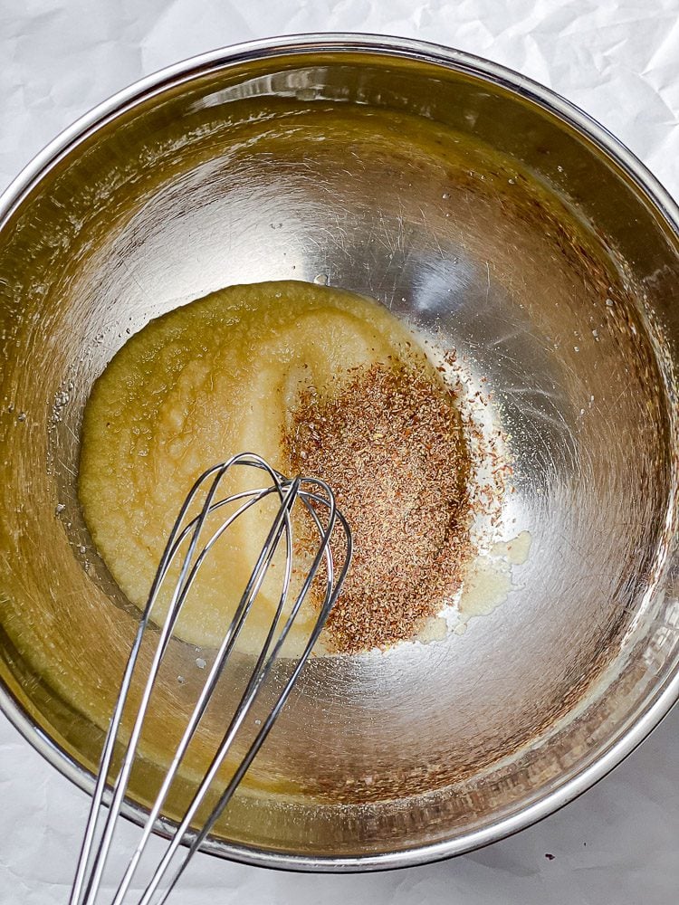 Flax meal being whisked into the wet ingredients in a large metal bowl.