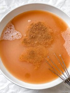 Ground cinnamon floating on the mixed juices in a large white bowl, with a whisk ready to stir.