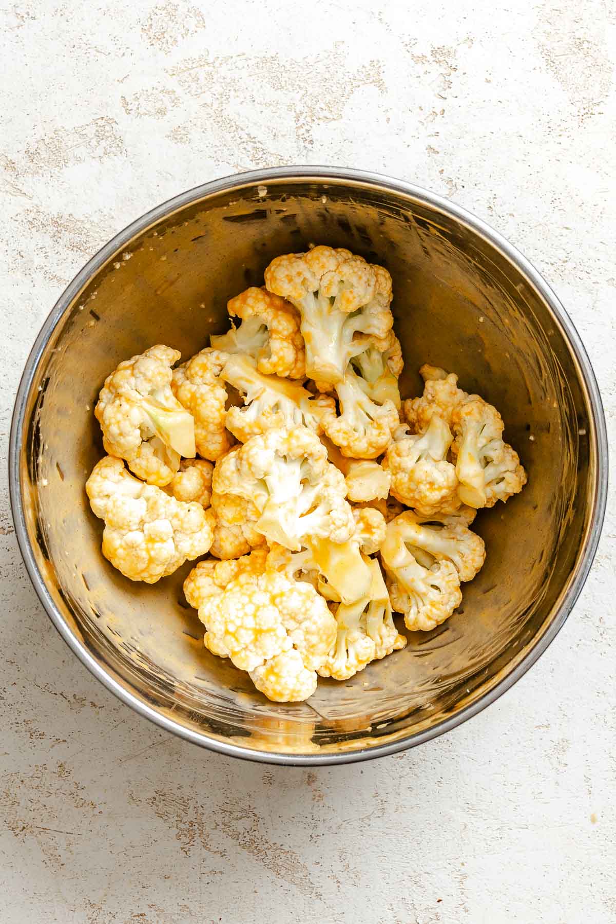 Process shot showing cauliflower added to bowl.