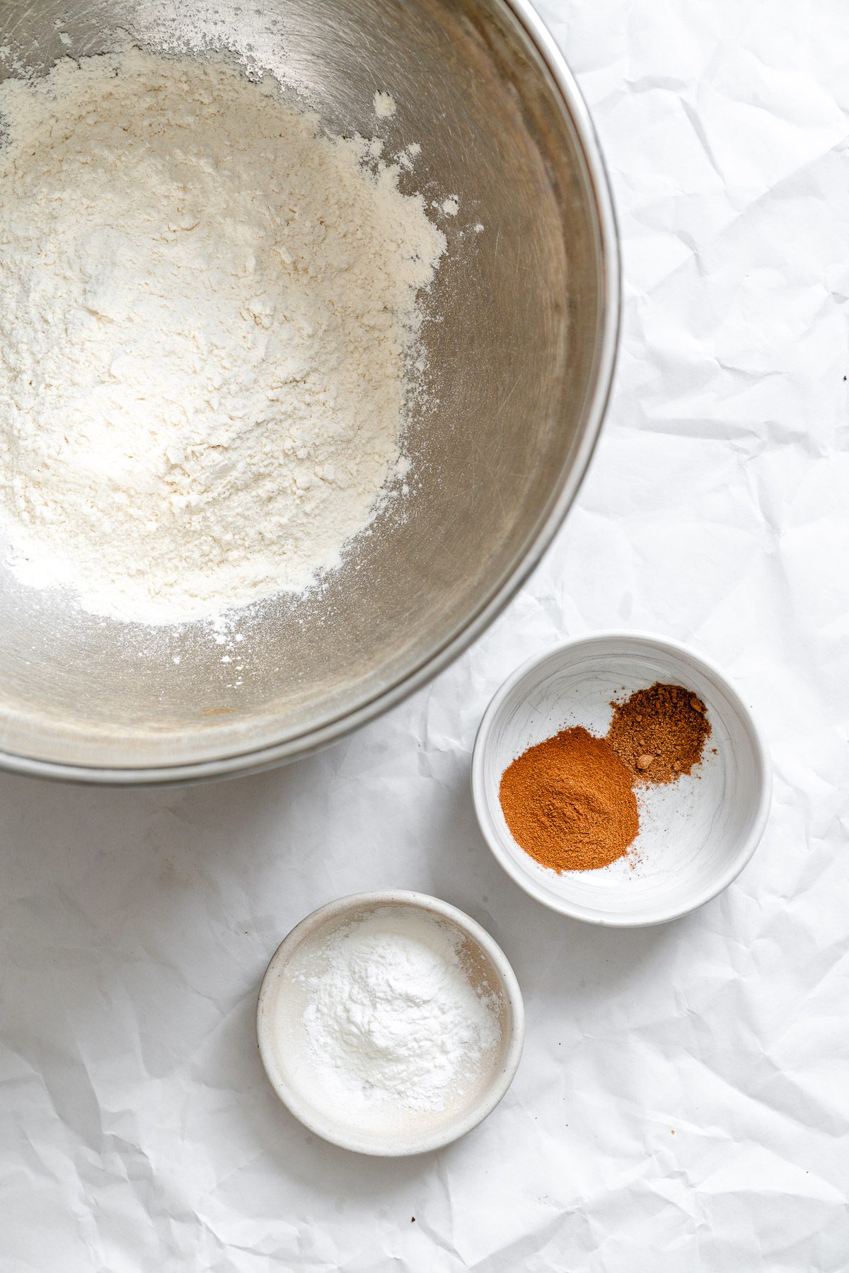 Process shot showing dry ingredients measured out in individual bowls on white surface.