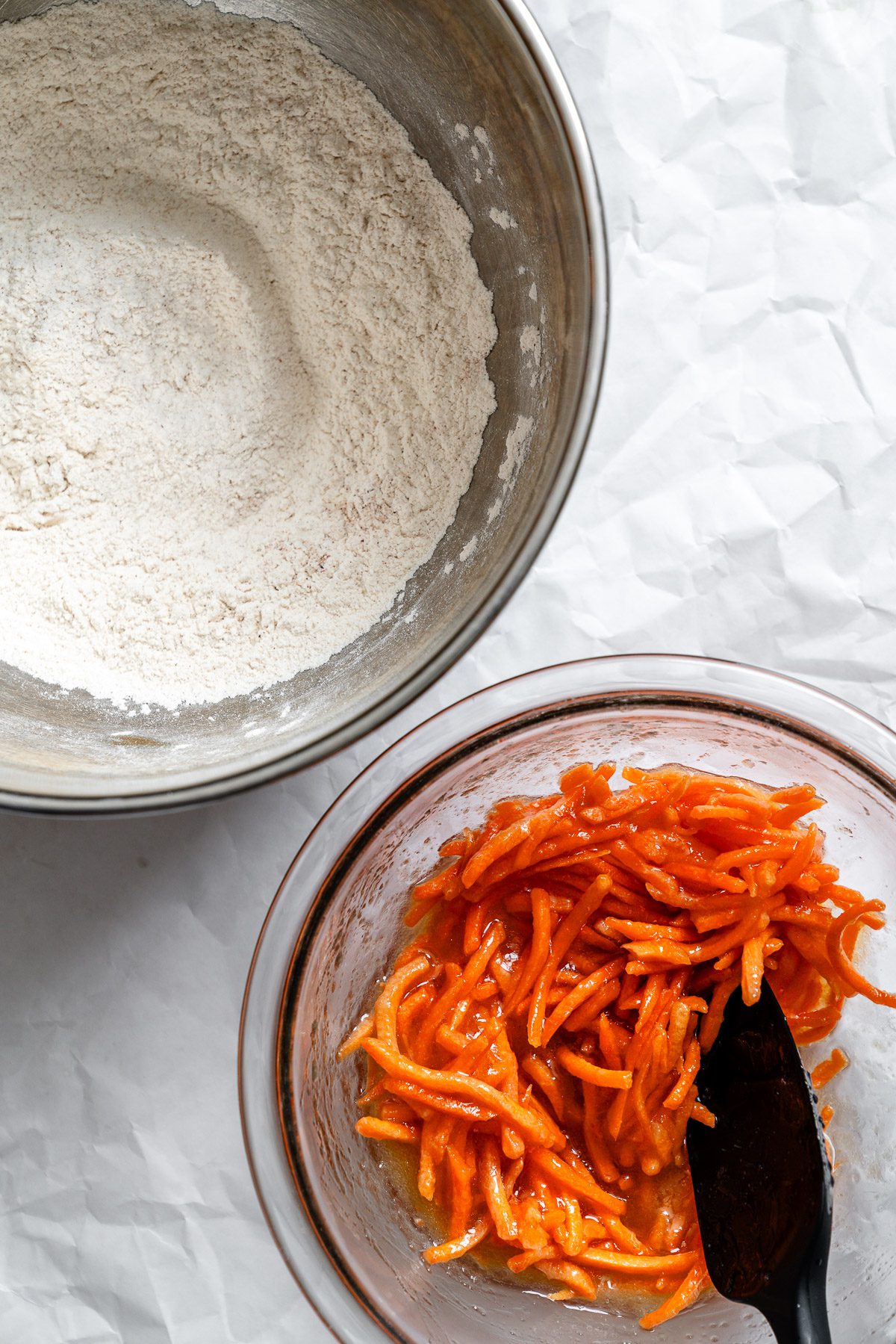 Process shot showing bowl of mixed ingredients alongside a bowl of carrots.