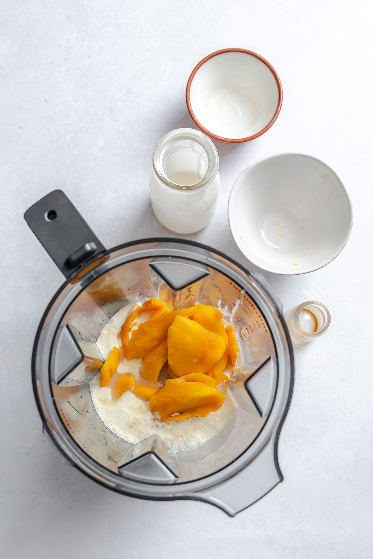 Process shot showing ingredients for Vegan Mango Ice Cream (Ninja Creami) in ninja creami machine.