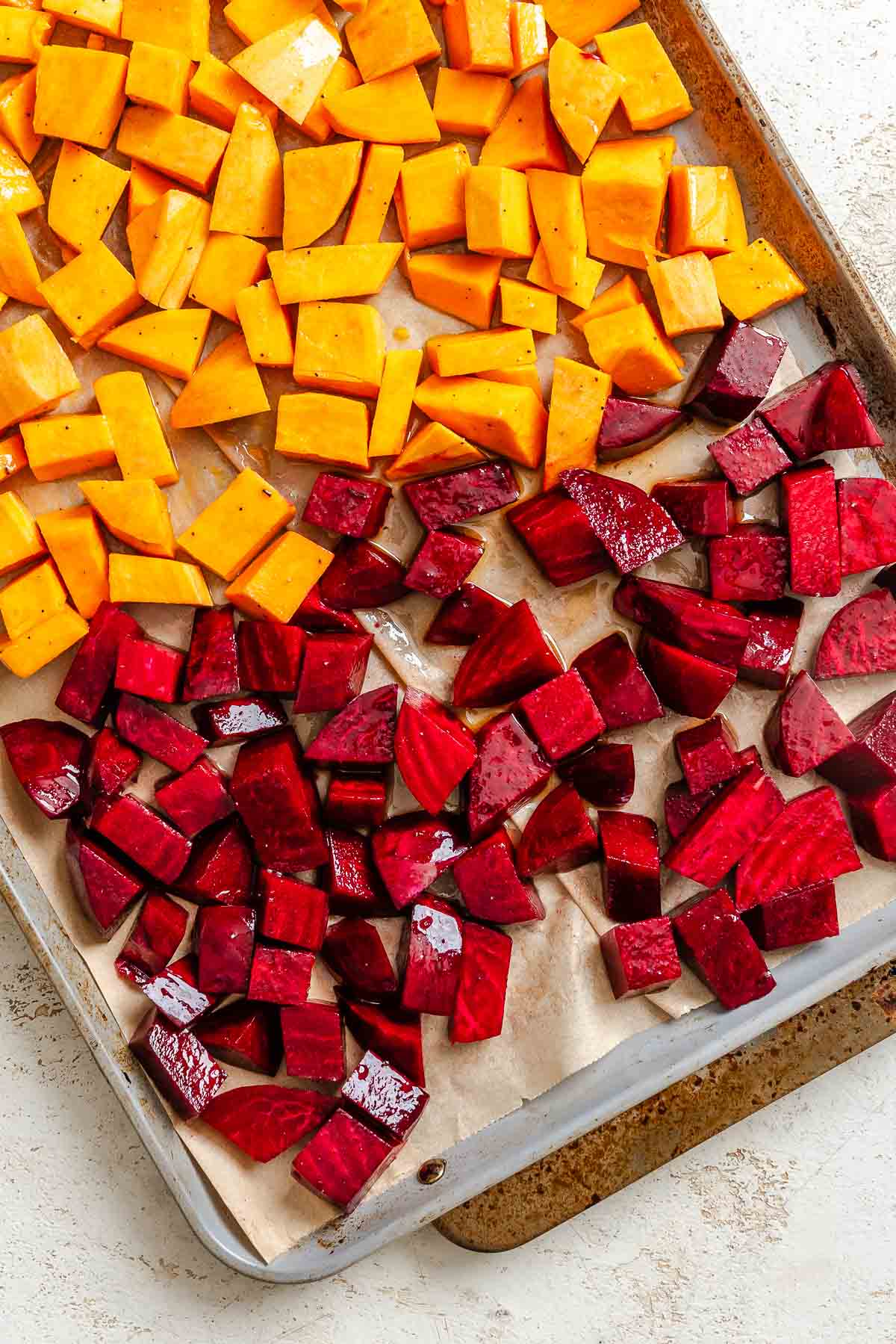 Process shot showing beets and sweet potato on baking dish.