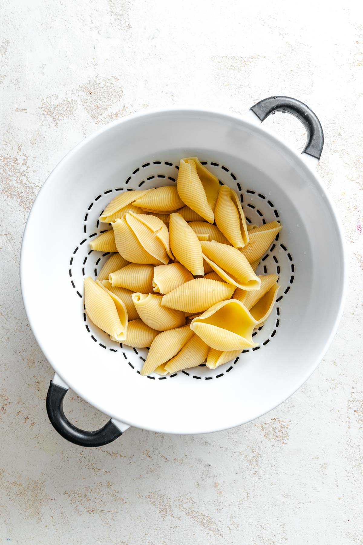 Process shot showing pasta shells in strainer.
