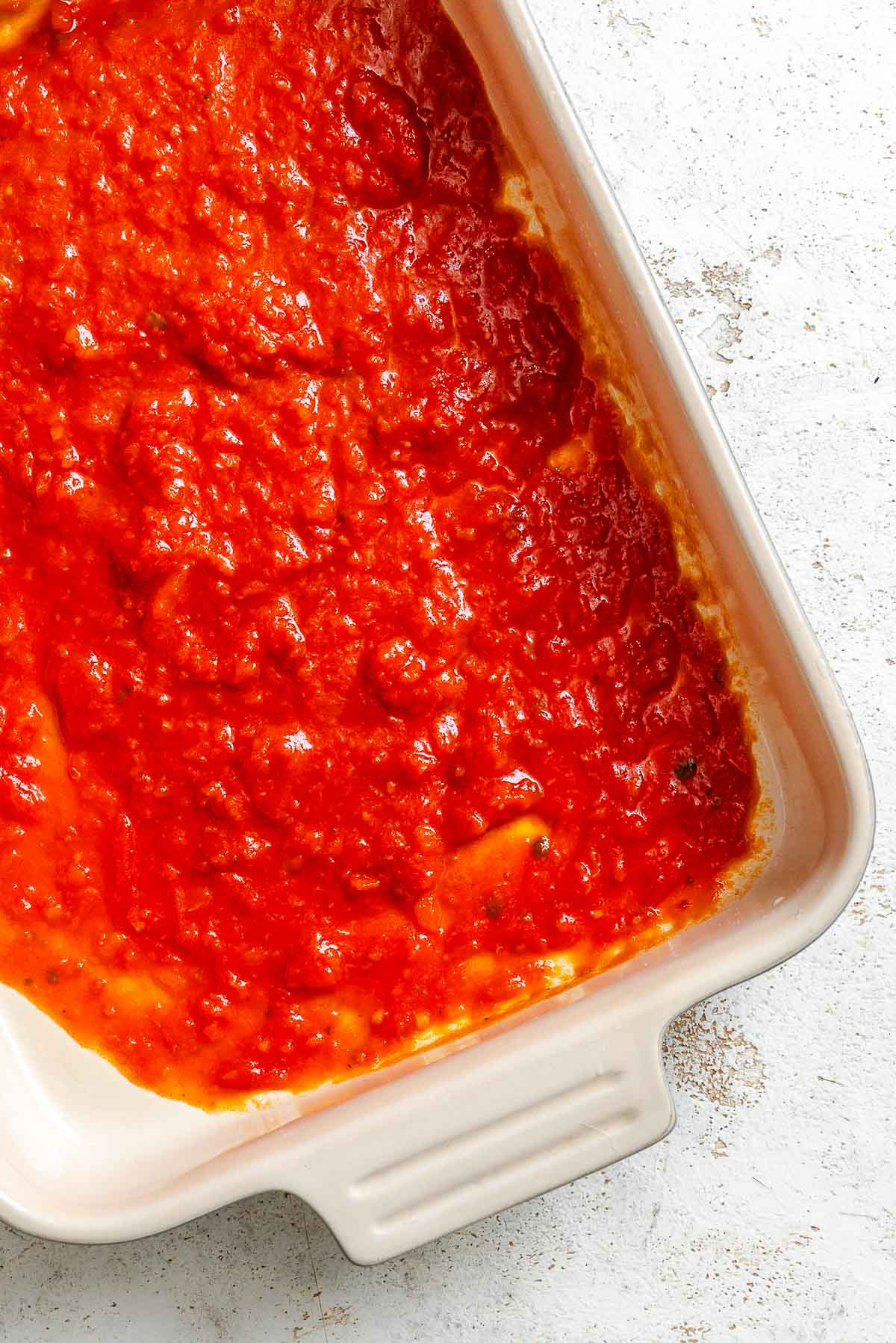 Process shot showing layer of sauce added to baking dish.