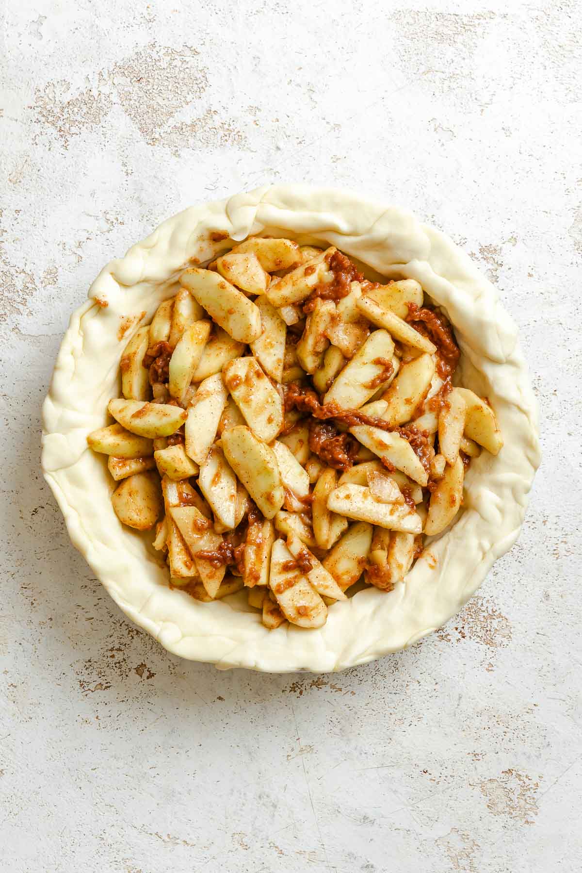 Process shot showing apples added to pie crust.