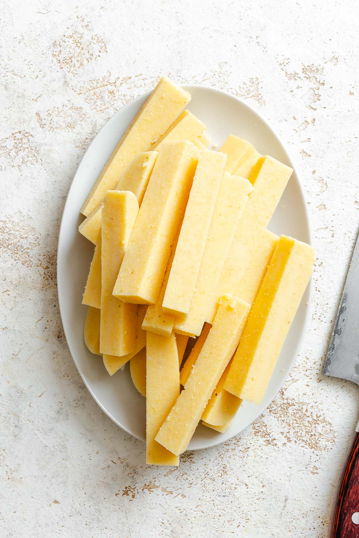 Process shot showing polenta cut into fries shape on white platter.