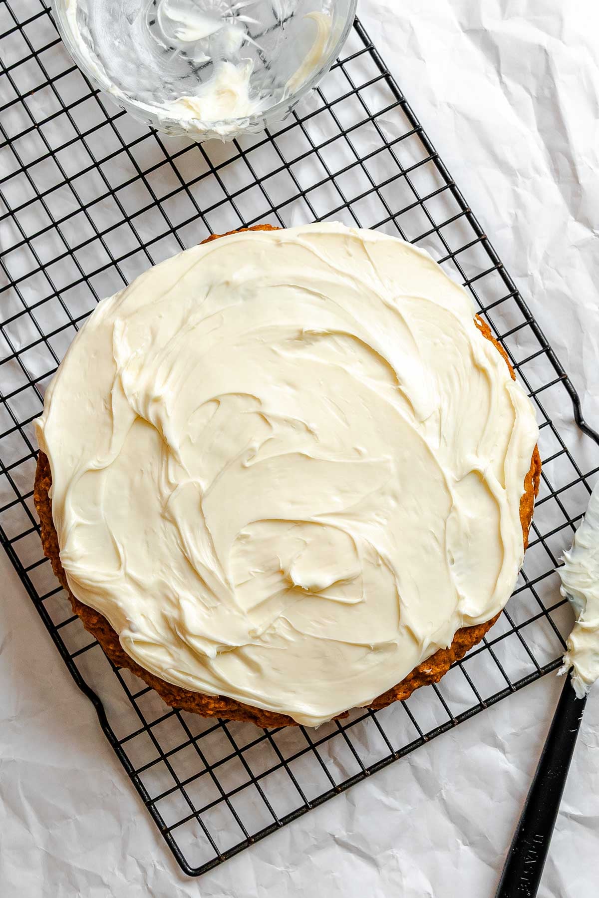 Process shot showing adding vegan cream cheese frosting to cake.