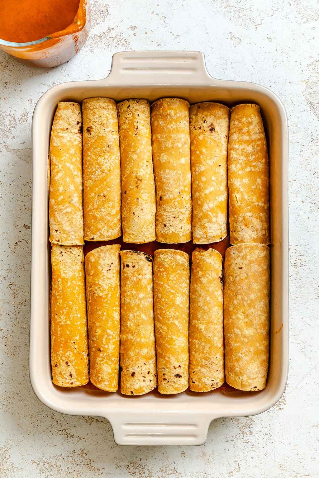Process shot showing vegan enchiladas added to baking dish.