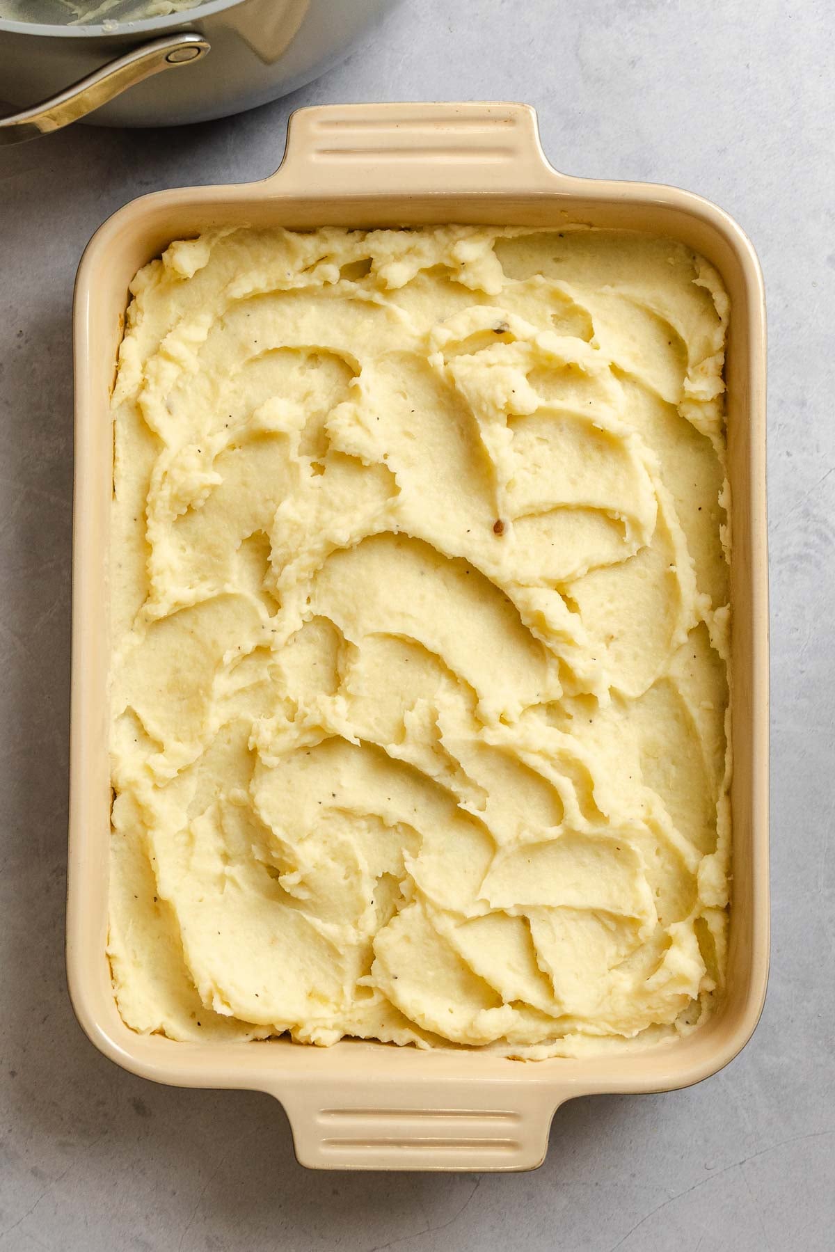 Process shot showing mashed potatoes spread on baking dish.