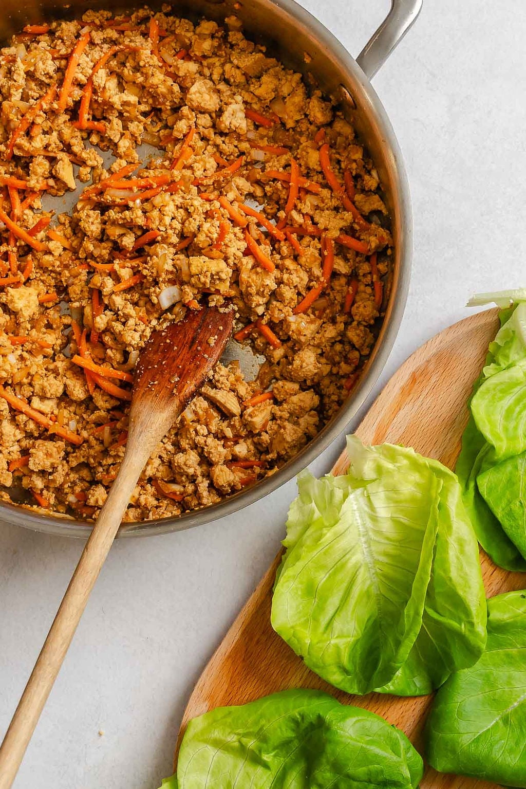 Process shot showing tofu mixture cooking in a pan alongside lettuce.