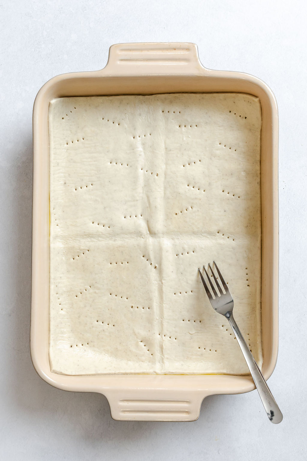 Process shot showing poking holes in puff pastry in baking dish.
