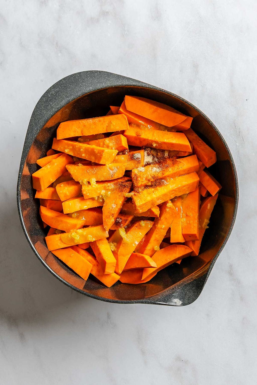Process shot showing mixing spices and sweet potatoes in a bowl.