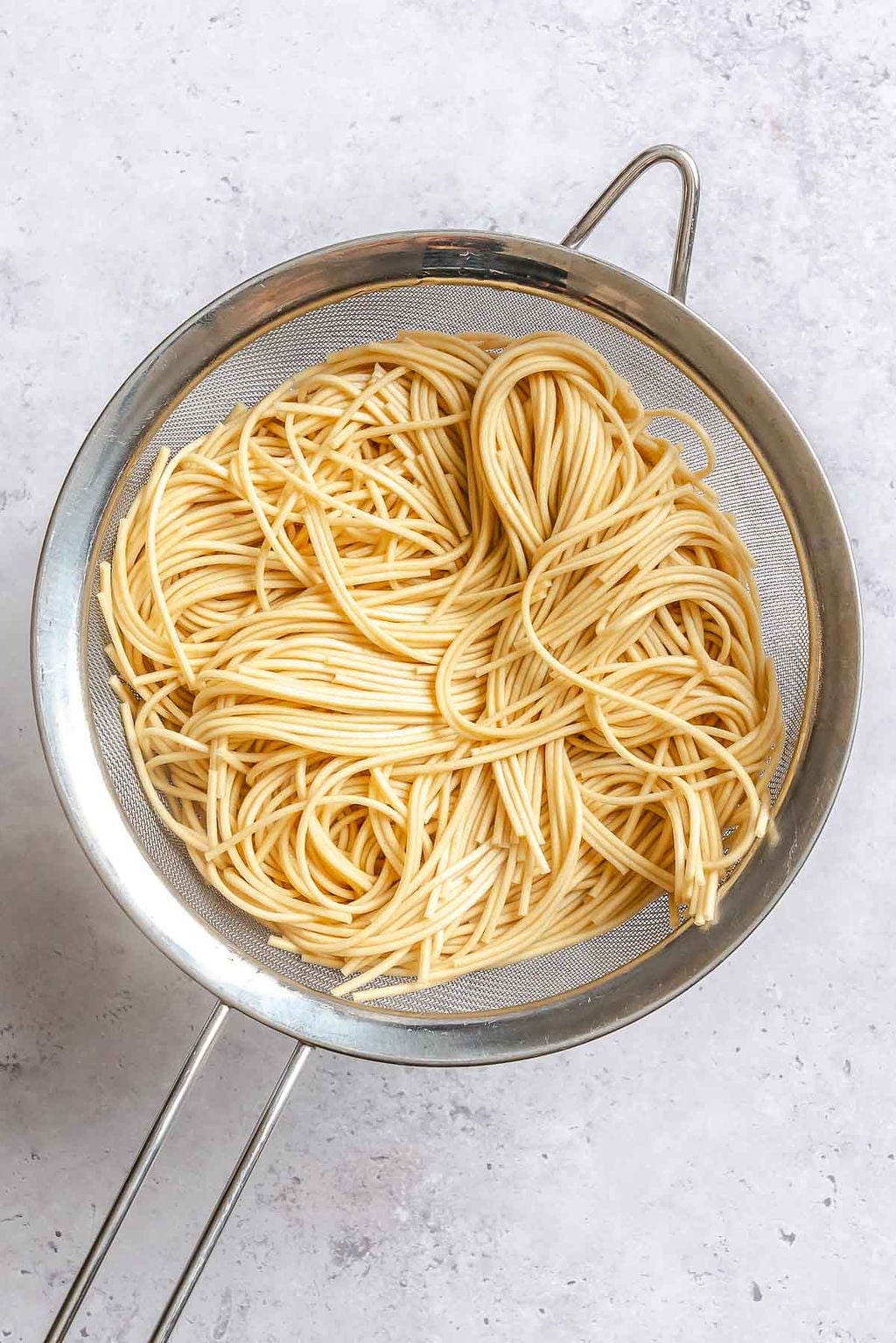 Process shot showing noodles in a strainer.